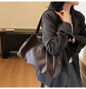 Detail of large brown pebble leather tote bag with gothic metal cross and chain ornament