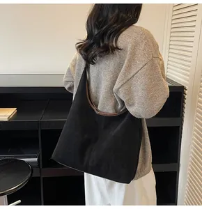 Detail of minimalist black faux suede tote bag with brown leather trim worn by model