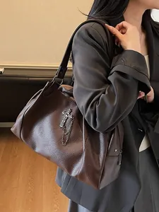 Brown leather tote bag with cross pendant and chain detail shown on shoulder for daily commute