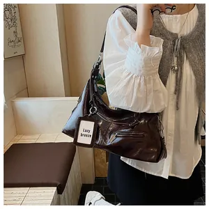 Detail of glossy espresso brown pleated underarm bag with silver hardware and pendant