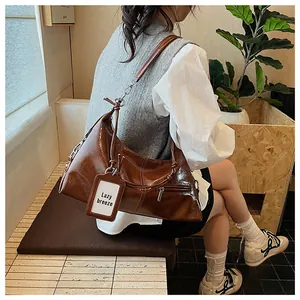 Close-up of a glossy brown shoulder bag featuring a zipper and a white decorative tag