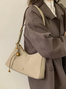 Chic beige underarm bag in matte leather featuring a gold sphere charm and metal plaque