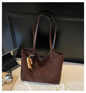 Detail of dark brown suede tote bag featuring a beaded charm on a white desk