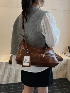 Brown faux leather shoulder bag with glossy finish shown on model in warm studio light