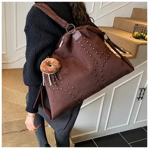 Detail der braunen Wildleder-Tragetasche mit Metallnieten und Plüsch-Donut-Anhänger