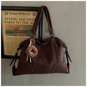 Détail d'un sac cabas en daim marron avec des clous argentés et un charme en peluche
