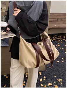 Detalle de un bolso tote grande de lona beige con correas de cuero marrón en una calle