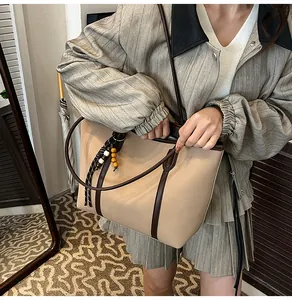 Detail of a large beige tote bag with brown contrast trim and a wooden bead charm