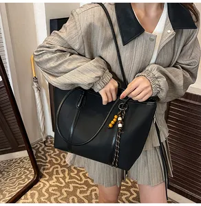 Detail of black faux leather tote bag featuring elegant beaded charm and long shoulder straps