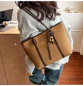 Detailed view of khaki brown tote bag with dark leather trim and vintage wooden bead charm