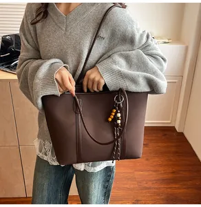 Detailed close-up of dark brown tote bag featuring ethnic beaded charm and matte texture