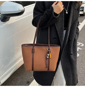 Brown large-capacity tote bag with beaded tassel detail worn on shoulder in street setting