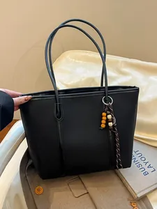 Classic black leather tote bag with wood bead tassel on a brown coat background