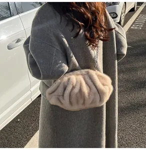 Close-up of beige plush pleated cloud bag with silver chain strap on a grey coat