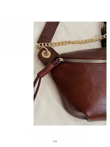 Close-up of dark brown leather texture with smooth zipper and golden metal chain strap