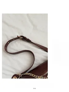 Close-up of dark brown leather crossbody bag featuring gold metal buckles and chain strap