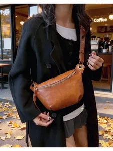 Brown faux leather half-moon crossbody bag with wide strap in an autumn street setting