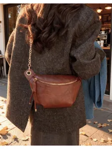 Brown leather half-moon bag with gold chain strap and fringe zipper detail on a coat