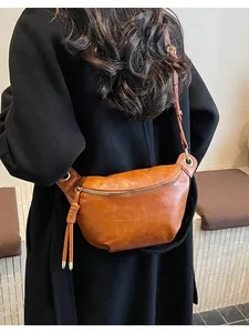 Brown leather moon bag detail with zipper closure and tassel decor on a black coat