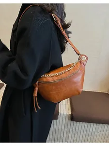 Brown leather half-moon crossbody bag with gold chain and tassel on black coat