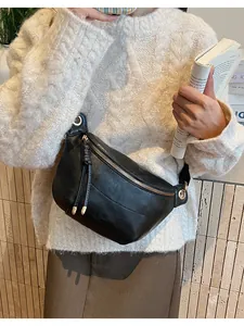 Detail of black faux leather crossbody bag showing gold zipper and woven pull tab texture