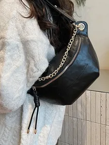 Chic black faux leather crossbody bag with chunky gold chain strap worn on white sweater