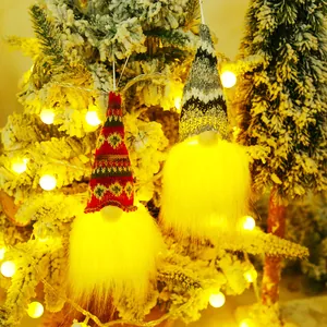 Set of two glowing Christmas gnomes with knitted hats hanging on a snowy Xmas tree