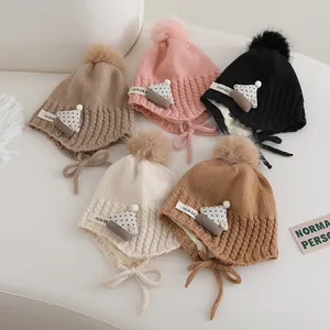 Flat lay view of knitted baby beanies with pompoms and earflaps in five assorted colors