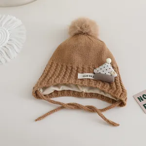 Detail view of brown knit baby hat with pompom and (G)I-DLE woven label on side