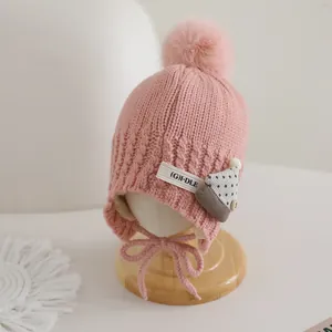 Detailed knit texture and plush pom-pom on pink children winter hat with ear flaps