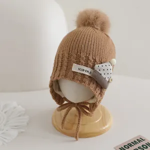 Close-up of warm brown baby knit hat with faux fur pompom and decorative logo patch