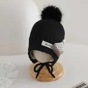 Close-up of black knit kids hat with fluffy pompom and (G)I-DLE patch detail