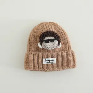 Dettaglio del berretto in maglia caramello con patch bambola e etichetta Bonjour