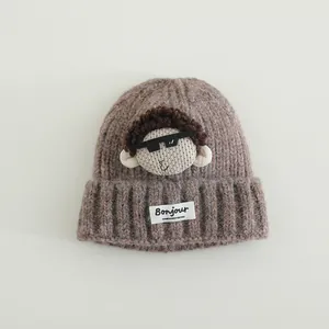 Dettaglio del cappello in maglia marrone con bambola riccia ed etichetta Bonjour