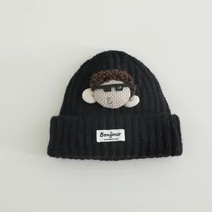 Dettaglio del cappello nero in maglia con patch di bambola e etichetta Bonjour