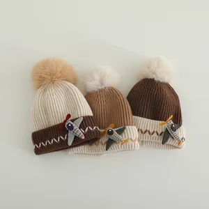 Detail van gebreide wintermutsen voor baby's met een 3D-vliegtuigpatch en een zachte pompon