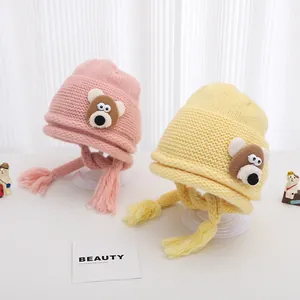 Winter knitted baby hat with cute cartoon bear patches and braided earflaps in pink and yellow
