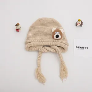 Detail of baby knit hat with brown bear patch and tassels on soft beige fabric