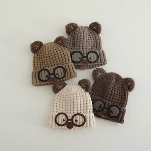 Close-up of four knitted children's bear hats in neutral tones with cute glasses patches