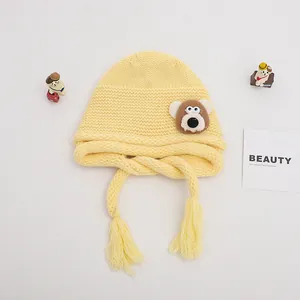Detailed texture of yellow knitted baby hat featuring brown bear patch and tassels