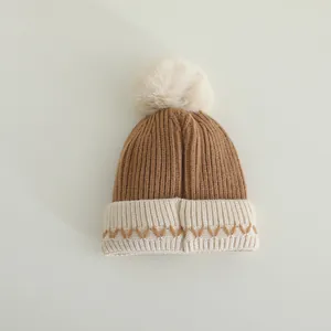 Detail van gebreide kindermuts met witte pompon en bruin golfpatroon voor winter