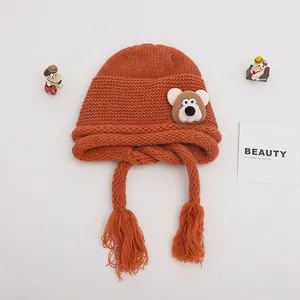Detail of ginger orange knit baby hat featuring cute bear patch and braided tassels