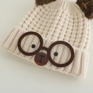 Chic beige knitted kids hat with brown ears and decorative glasses for winter warmth