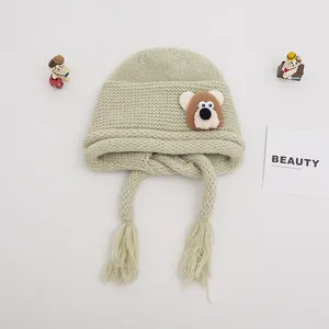Close-up of light green knit baby hat with earflaps, tassels and cute bear patch