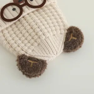 Close-up of knit baby beanie featuring cartoon cat ears and round glasses embroidery