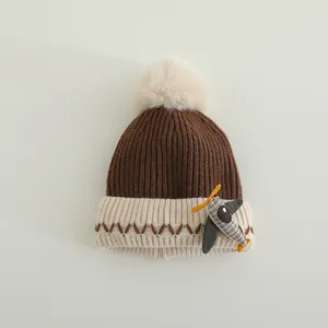 Detail van gebreide babymuts met schattig stoffen vliegtuigje en pluizige pompon