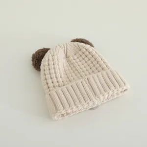 Detail of a beige knit beanie with brown pom-poms and thick textured material