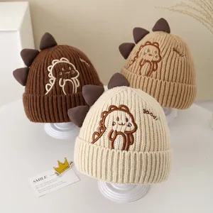Three warm knitted dinosaur baby hats in brown, khaki and cream with cartoon embroidery