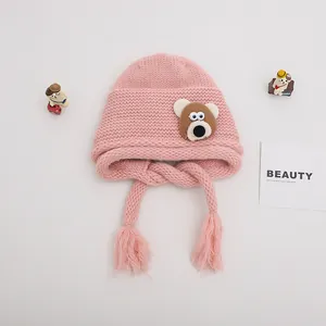 Detail of pink knitted baby hat with brown bear patch and tassels on soft gray background