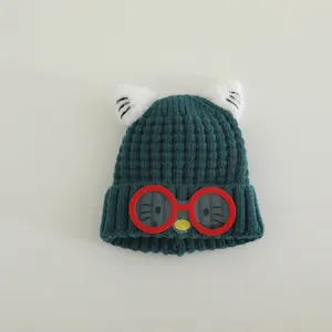 Detail of dark green knit hat with red glasses patch and cat ear accents for kids